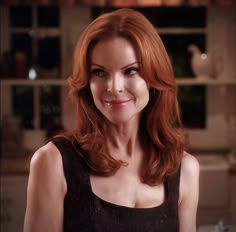 a woman with red hair is smiling at the camera and wearing a black dress in a kitchen