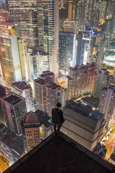 a man standing on top of a tall building in the middle of a city at night