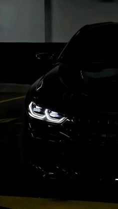 the front end of a black car with its lights on in a dark garage area