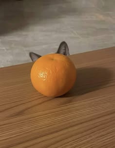 an orange sitting on top of a wooden table next to a cat's head