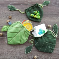 two green leaf shaped bags with buttons and thread on the sides, one has a card in it