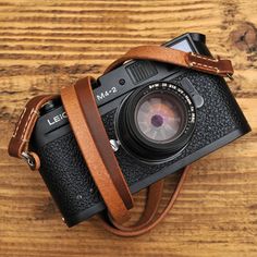 an old camera sitting on top of a wooden table next to a brown leather strap