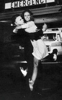 black and white photograph of two people hugging each other in front of an ambulance truck