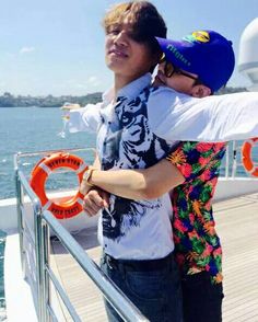 a man holding a young boy on top of a boat near the ocean and water