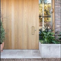a large wooden door sitting next to a planter filled with potted plants in front of a brick building