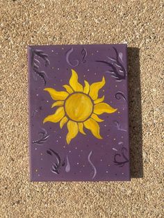 a purple tile with a yellow sun painted on it's side in the sand