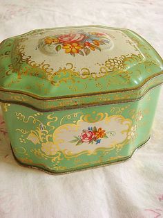 a green and white box sitting on top of a tablecloth covered bed with pink flowers