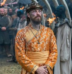 a man in an orange and gold outfit standing next to other men with fire behind him
