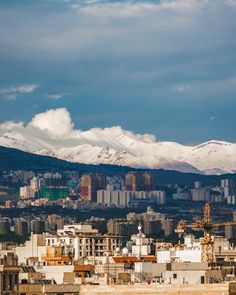 snow covered mountains are in the distance behind a cityscape with buildings and skyscrapers