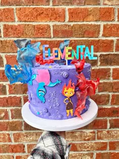 there is a purple cake with cartoon characters on it and the words'essential'spelled in rainbow letters