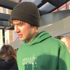 a young man wearing a green hoodie is looking at his cell phone while standing in front of a building