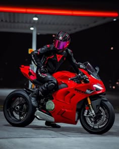 a person on a red motorcycle in a parking lot at night with the lights on