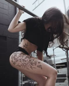 a woman in black shirt and shorts holding a pole with tattoos on her back legs