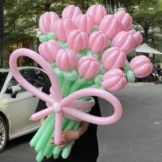 a woman holding a bunch of pink and green balloons in front of a white car