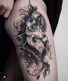 a woman's thigh with a black and white tattoo design on it, featuring a wolf