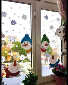 two snowmen are hanging from the window in front of some potted plants and flowers