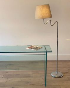 a glass table with a book on it and a lamp in the corner next to it