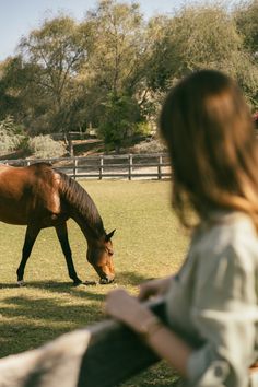a woman standing next to a brown horse in a field