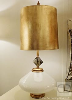 a white table with a gold lamp on it and a mirror in the back ground