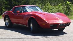 a red sports car is parked on the side of the road in front of some trees