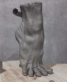 a sculpture of a hand with a pipe sticking out of it's foot on top of a wooden table