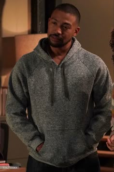the young man is wearing a gray hoodie and black pants, standing in front of a lamp