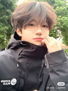 a young man in a black jacket is posing for the camera with his hand on his chin