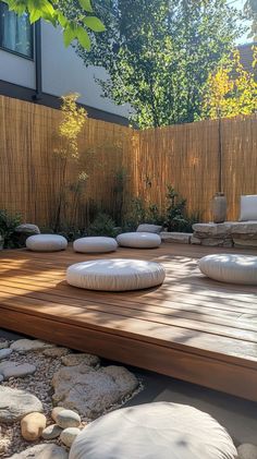 a wooden deck surrounded by white pillows and rocks in front of a bamboo privacy fence