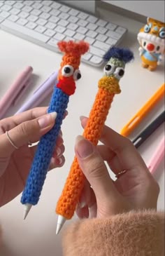 two crocheted pencils with eyes and nose are being held by someone's hands