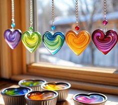 four muffin tins filled with different colored hearts hanging from chains on a window sill