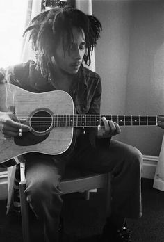 a man with dreadlocks sitting in front of a guitar and playing the guitar