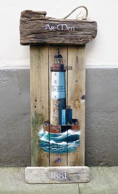 a wooden sign with a lighthouse painted on it's side next to a wall