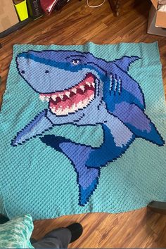 a crocheted shark rug is on the floor next to a person's feet