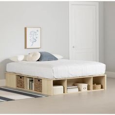 a bed with storage drawers underneath it in a white room next to a wall mounted door