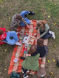 four people sitting on a blanket eating food