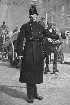 an old black and white photo of a man in uniform standing on the street with horse drawn carriages behind him