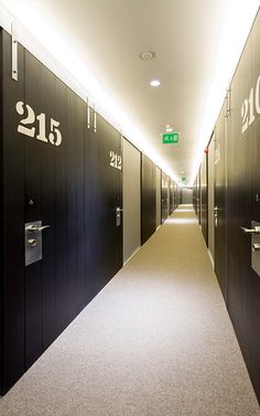 a long hallway with black doors and numbers on the walls, leading to an exit