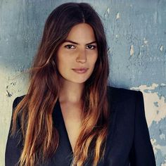 a woman with long hair standing in front of a blue wall wearing a black suit