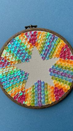 a colorful piece of art made out of buttons on a blue surface with a black hook