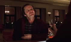 a man sitting at a table with a glass of wine in his hand looking up