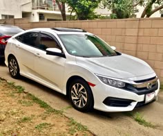 two white cars parked next to each other on the side of a road in front of a brick wall
