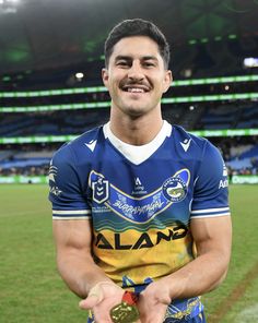 a rugby player holding a gold medal in his right hand and smiling at the camera