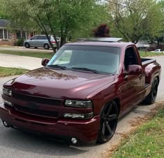 a red truck parked on the side of a road next to grass and trees in front of a house