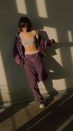 a woman leaning against a wall with her hands on her hips wearing purple jeans and a crop top