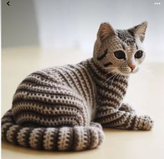 a knitted cat sitting on the floor looking off to the side with eyes wide open