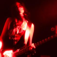 a woman holding a guitar in her hand and looking at the camera with red light behind her