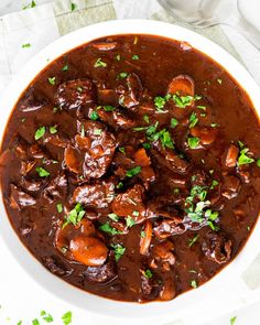 a white bowl filled with beef and mushrooms in gravy, garnished with parsley