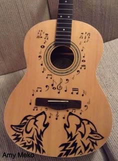 an acoustic guitar decorated with musical notes and wolf heads on it's neck, sitting on a couch