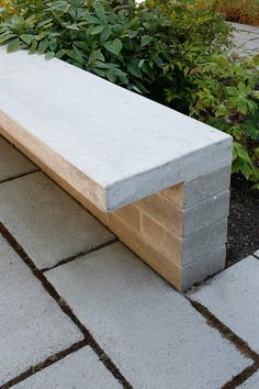 a concrete bench sitting on top of a brick walkway next to bushes and shrubbery