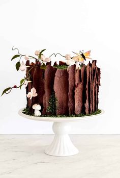 a chocolate cake with flowers and leaves on top is sitting on a white pedestal in front of a white wall